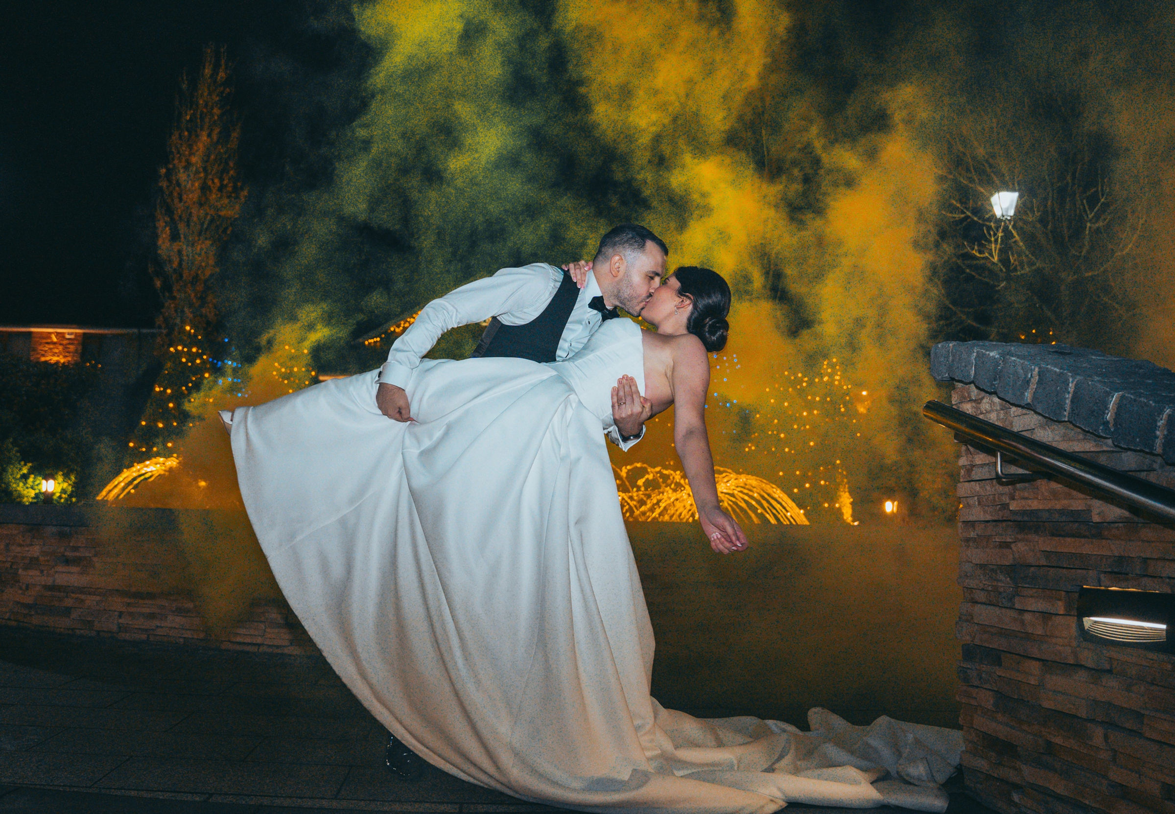 A newly married couple kissing as golden smoke rises behind them