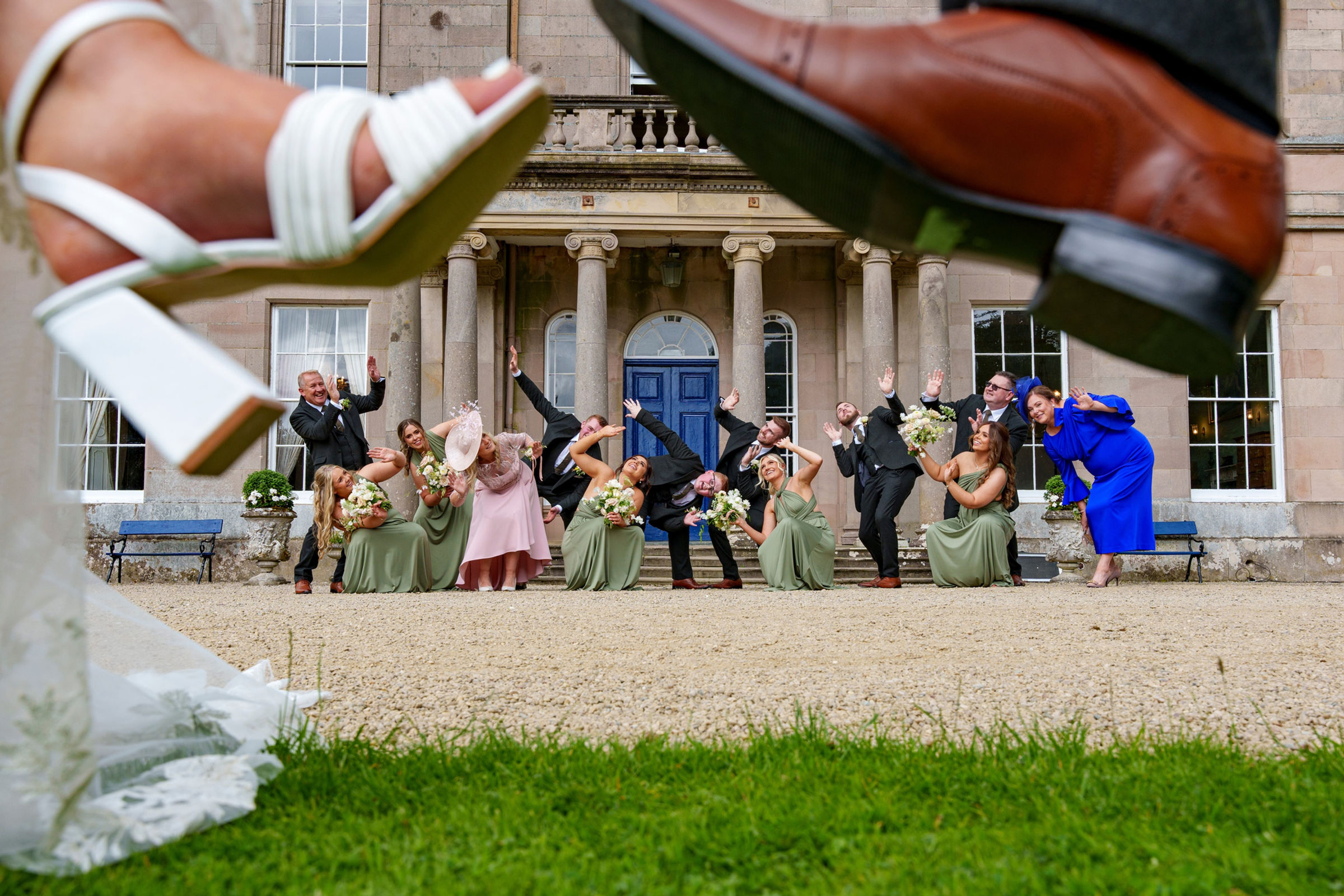 A wedding party framed between the newlyweds' shoes