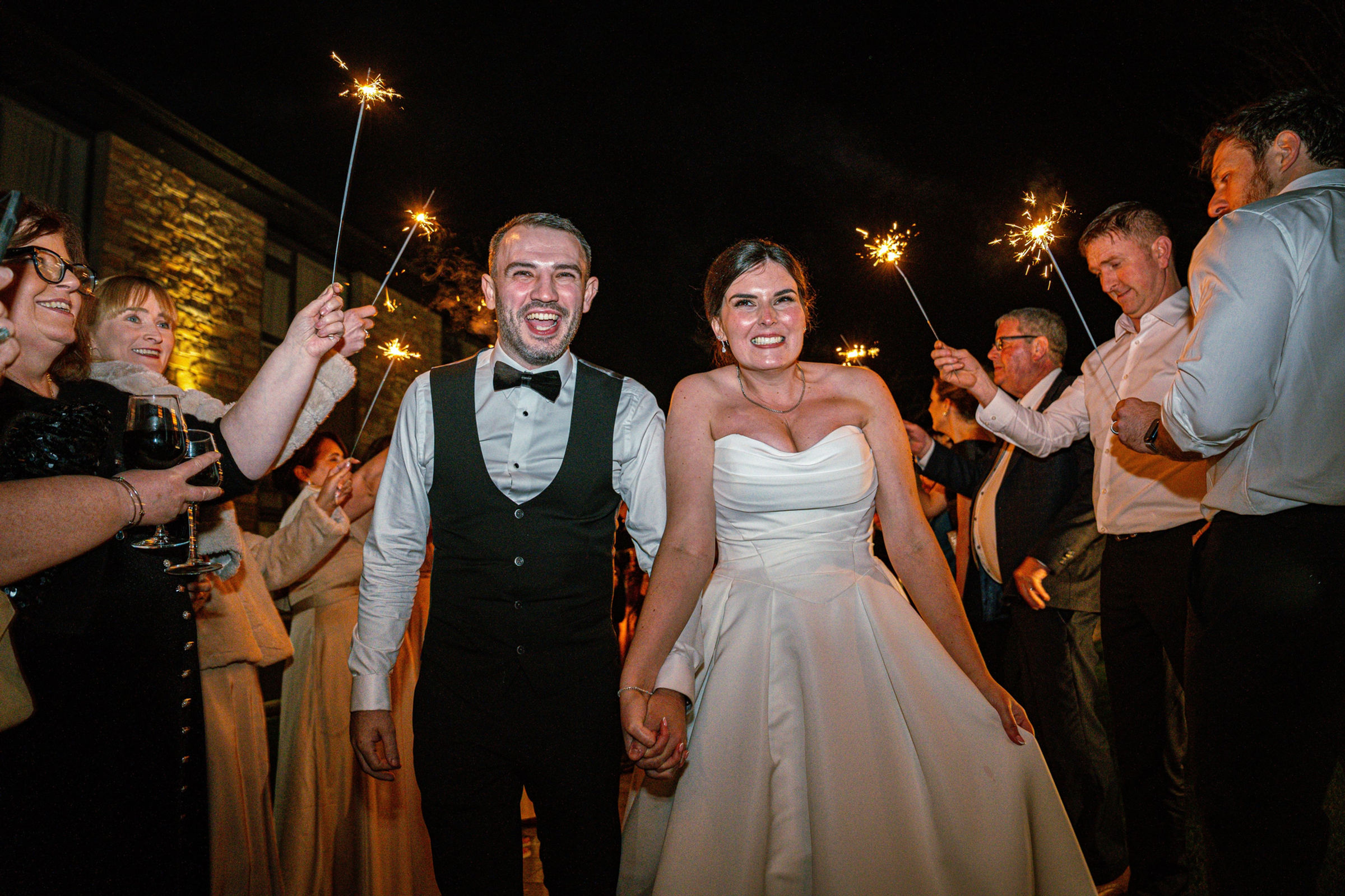 A newly married couple walking through sparklers with their friends
